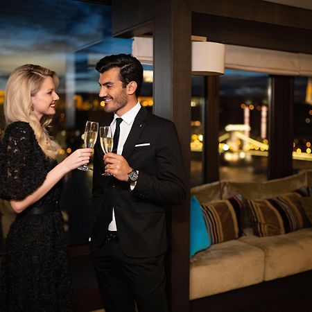 Intercontinental Budapest By Ihg Exterior foto The photo depicts a couple celebrating a special moment. The woman is wearing a stylish black dress and is holding a glass of champagne, while the man is dressed in a formal black suit and also holding a glass. They are smiling at each other in a war