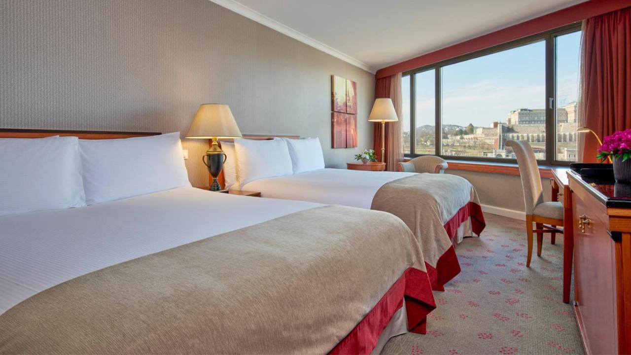 Intercontinental Budapest By Ihg Exterior foto The photo shows a hotel room featuring two twin beds with soft, light-colored bedding. There are bedside lamps on each side of the beds, and a decorative piece of artwork hangs on the wall. A window provides natural light and offers a view of the out