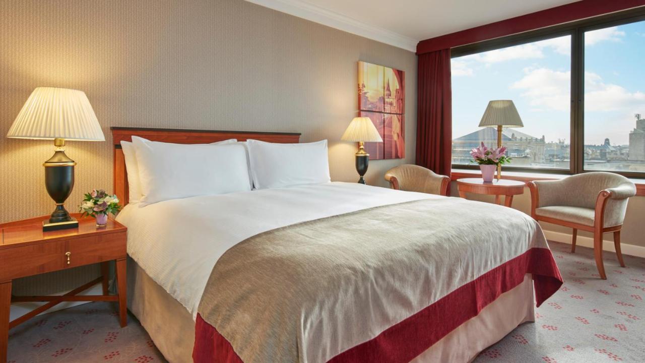 Intercontinental Budapest By Ihg Exterior foto The photo depicts a hotel room with a cozy and inviting atmosphere. There is a large bed with crisp, white linens, complemented by a decorative bedspread in a subtle color. On either side of the bed, there are bedside lamps providing soft lighting. 
