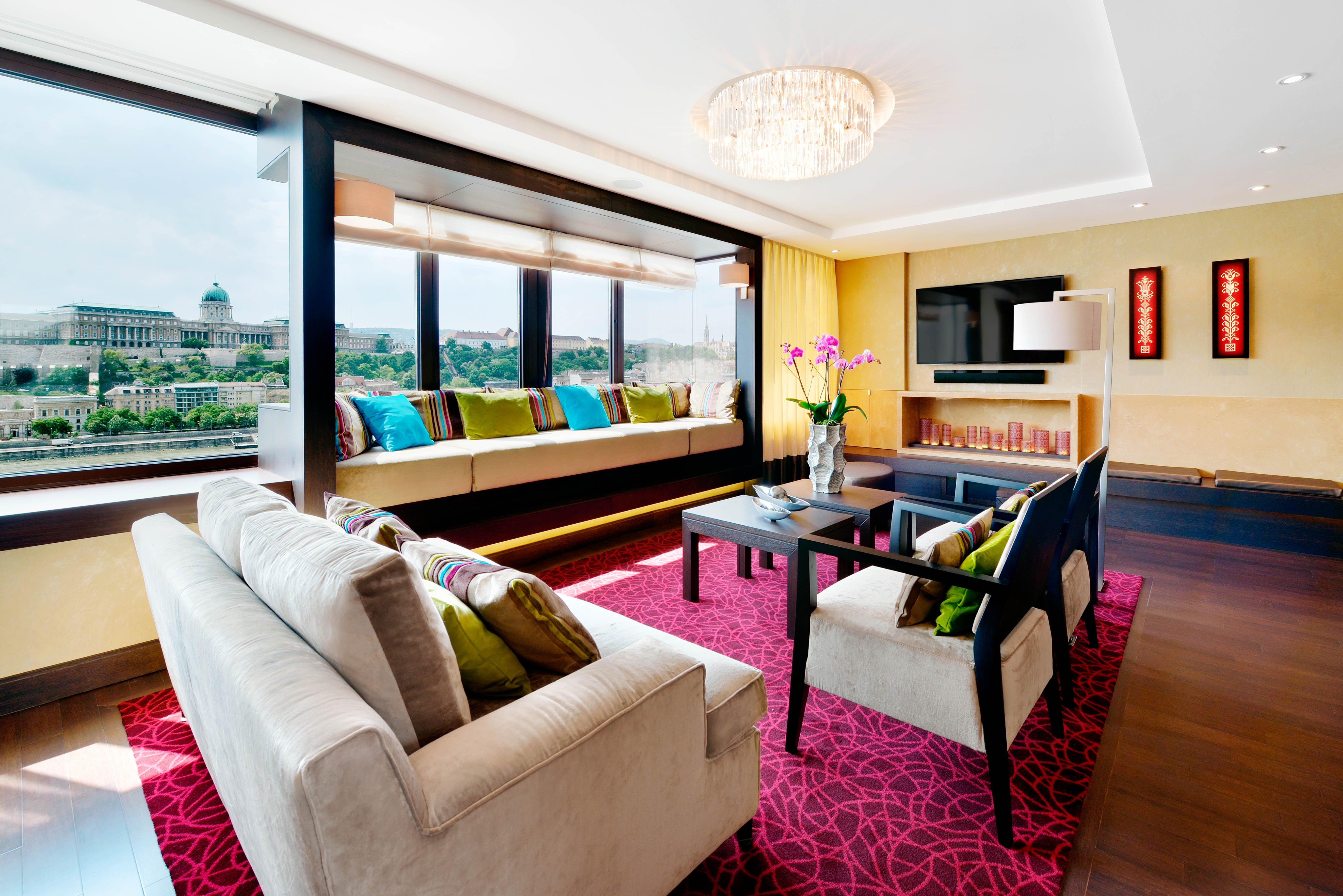 Intercontinental Budapest By Ihg Exterior foto The photo shows a modern and stylish living room with large windows that provide a view of the outside. The space features a neutral-colored sofa adorned with colorful pillows and a matching armchair. There is a dark wooden coffee table in the center