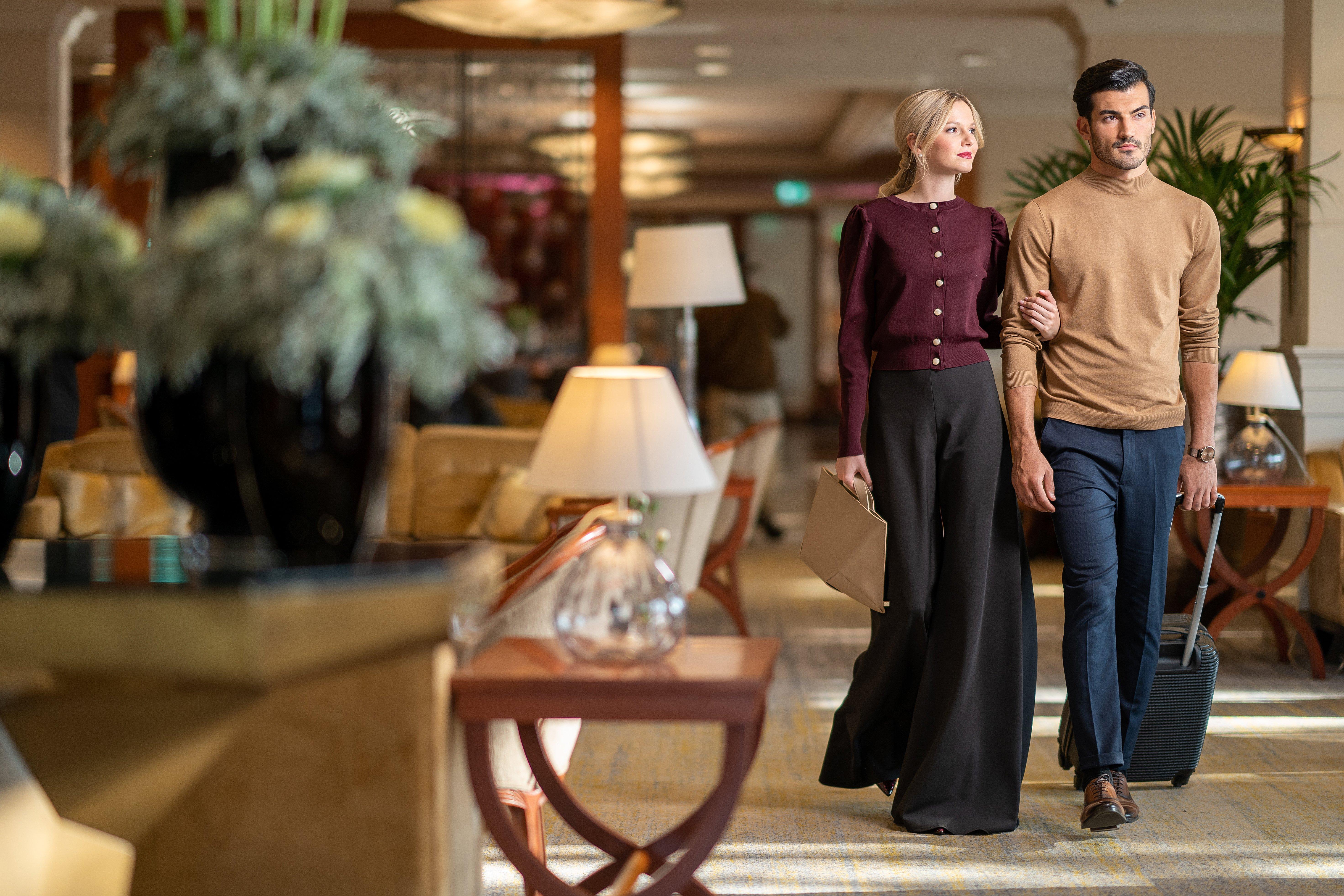 Intercontinental Budapest By Ihg Exterior foto The photo shows a stylish couple walking together in an elegant indoor setting, likely in a hotel or upscale venue. The woman is wearing a burgundy cardigan and wide-legged black trousers, while the man is dressed in a light brown sweater and dark je