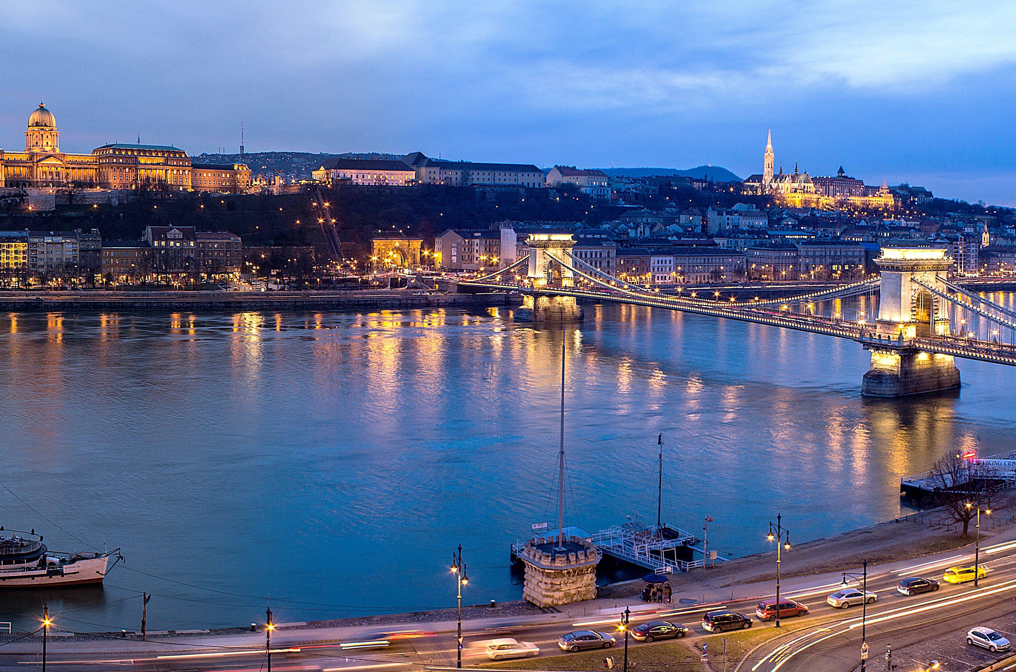 Intercontinental Budapest By Ihg Exterior foto The photo depicts a scenic view of a city, likely during twilight. In the foreground, there is a river that reflects the soft glow of lights from the surrounding structures. A prominent bridge spans the river, connecting two sides of the city. 

On o
