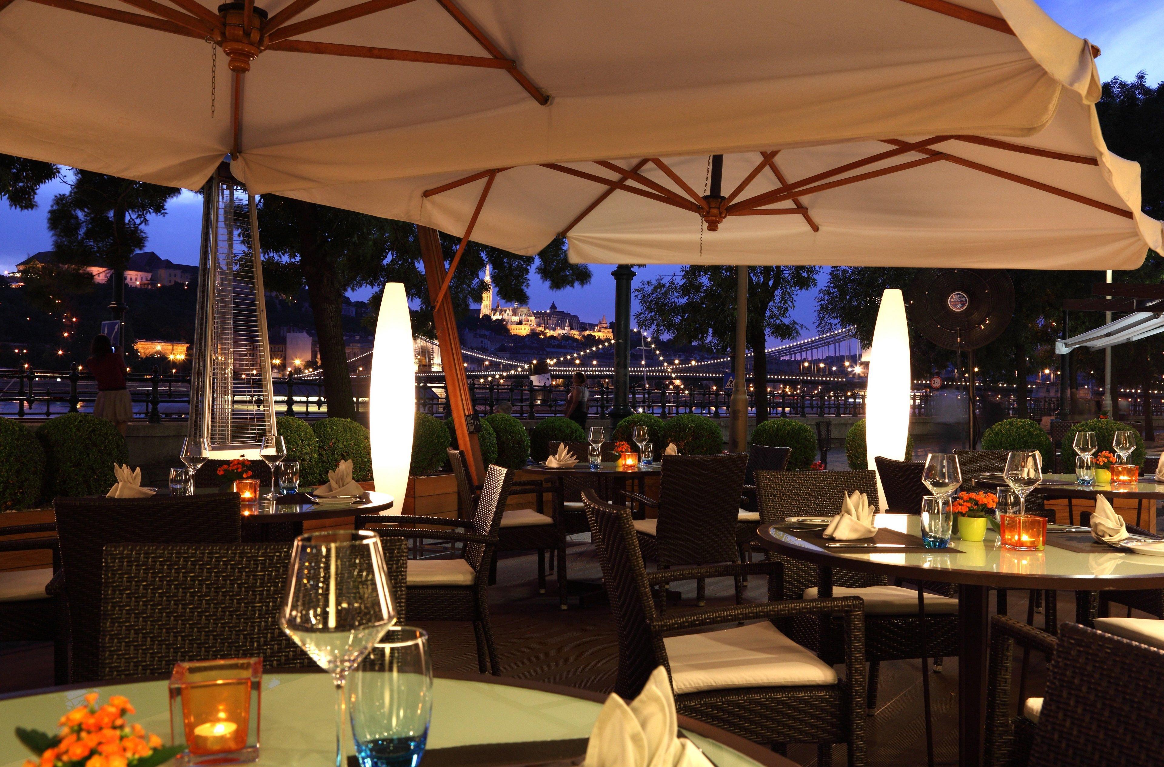 Intercontinental Budapest By Ihg Exterior foto The photo depicts an outdoor dining area at a restaurant, set up for evening service. There are several tables arranged with elegant place settings, including wine glasses and decorative napkins. The space is illuminated by soft lighting from candles