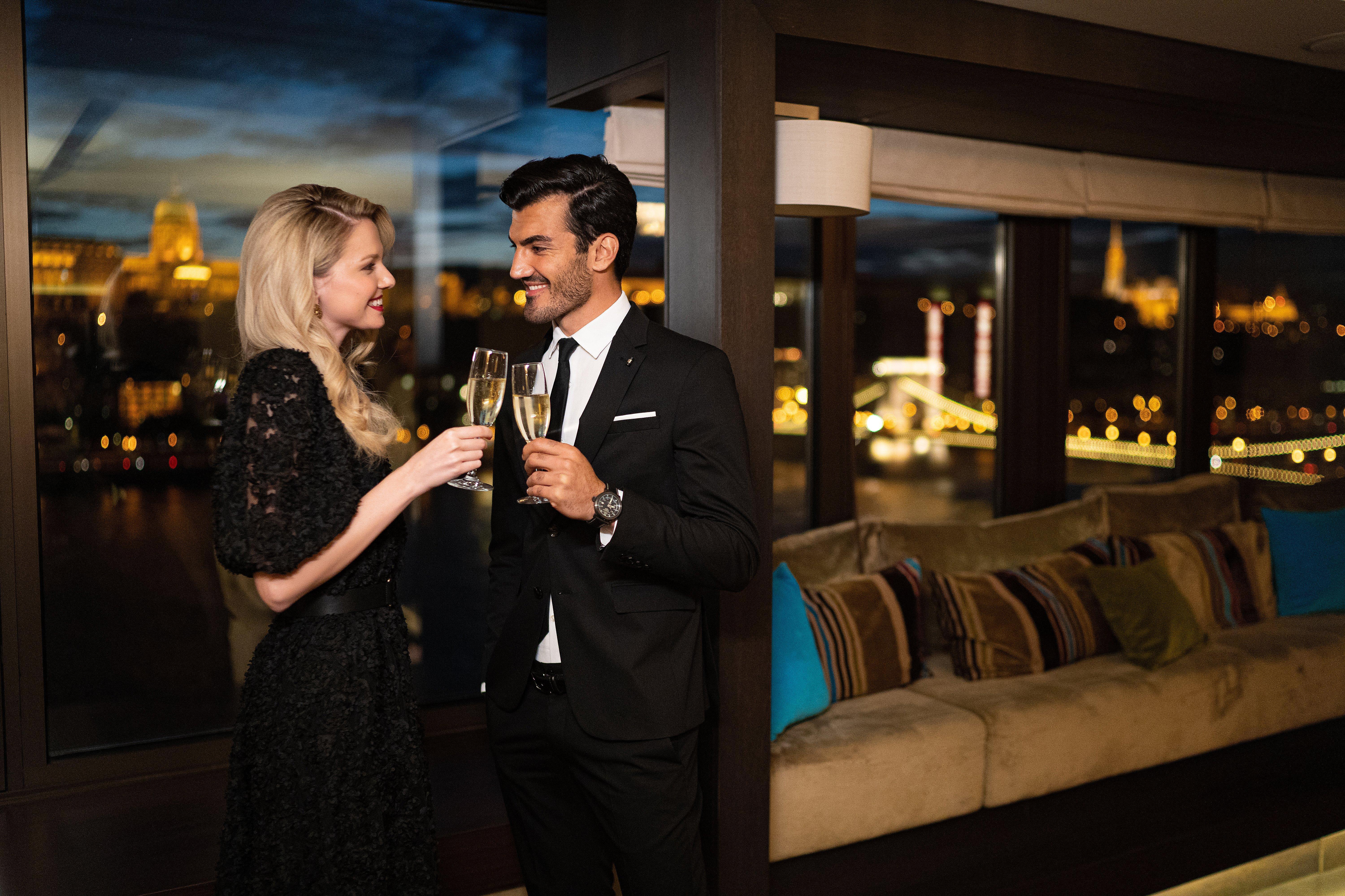 Intercontinental Budapest By Ihg Exterior foto The photo depicts a couple celebrating a special moment. The woman is wearing a stylish black dress and is holding a glass of champagne, while the man is dressed in a formal black suit and also holding a glass. They are smiling at each other in a war