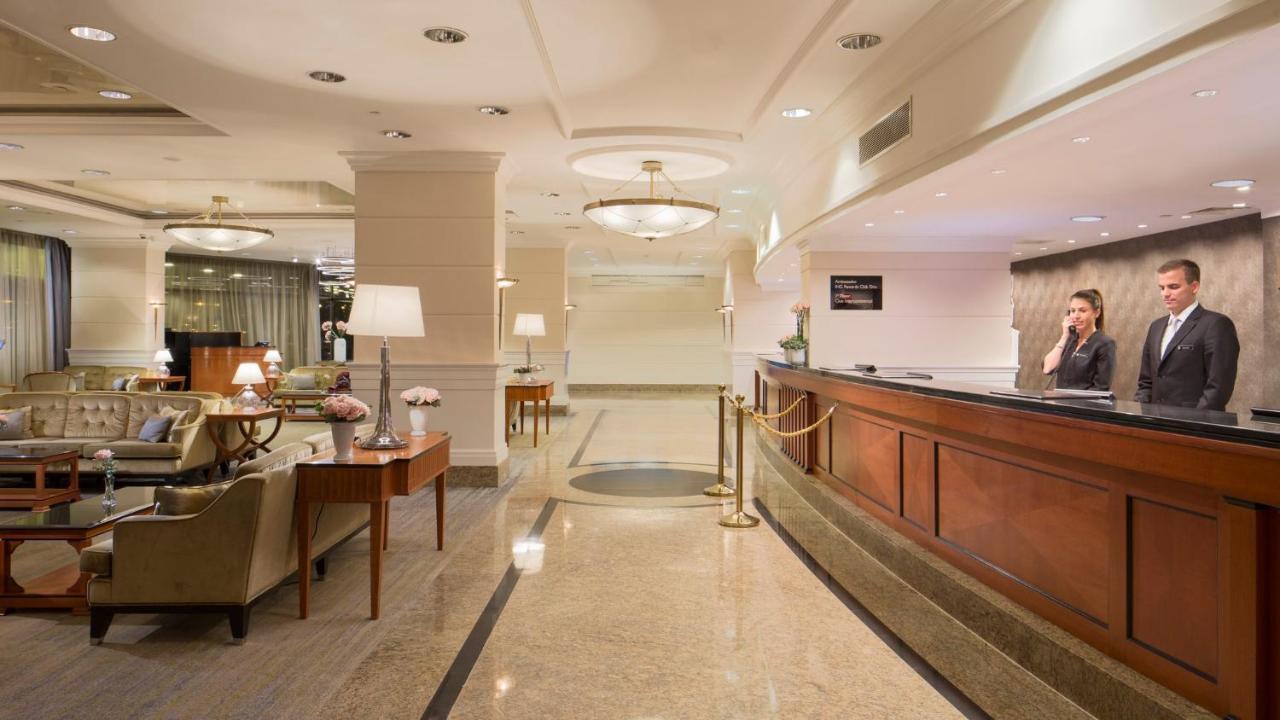 Intercontinental Budapest By Ihg Exterior foto The photo shows a hotel lobby featuring a reception area on the right side. The reception desk is made of dark wood, and there’s a staff member attending to guests. The lobby has elegant decor, with soft lighting from ceiling fixtures and table lamps