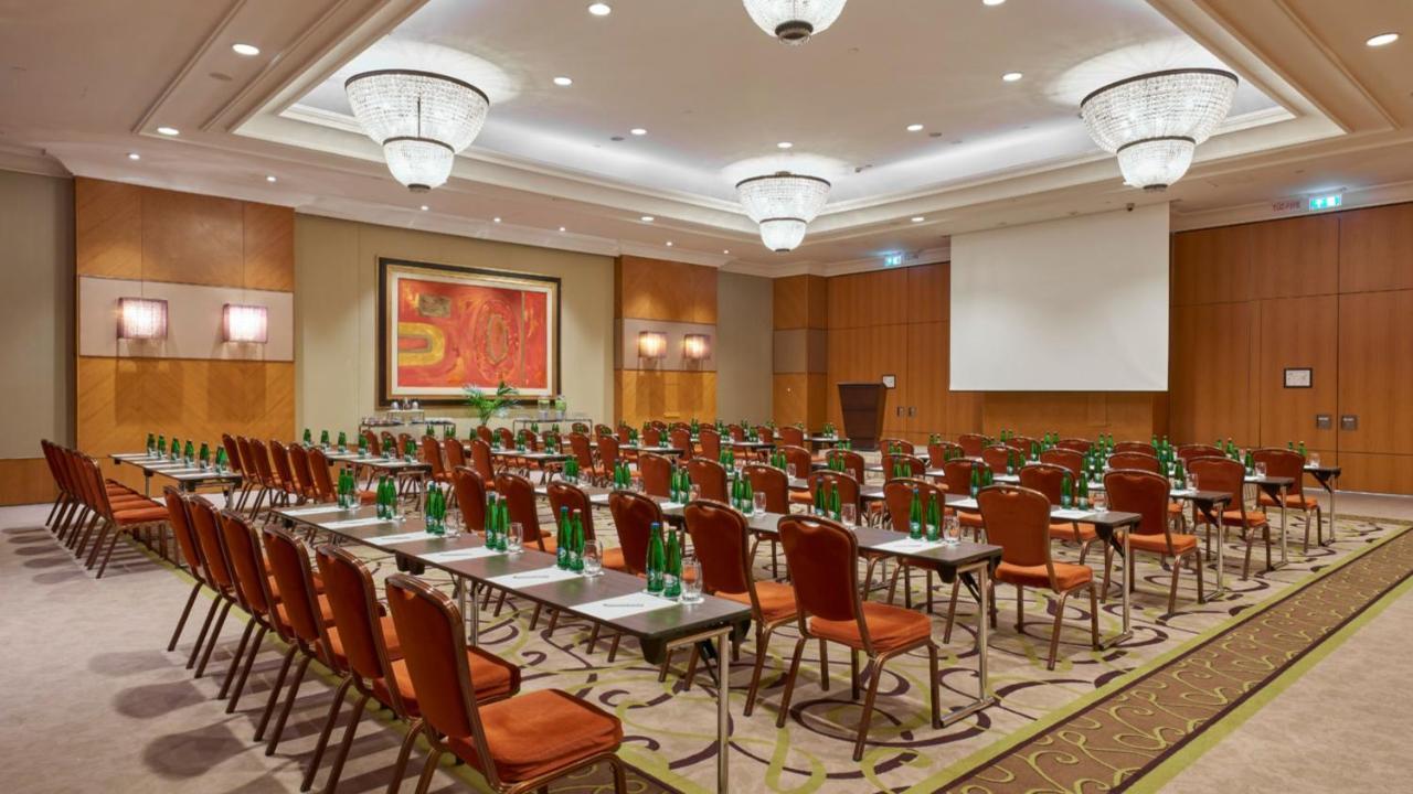 Intercontinental Budapest By Ihg Exterior foto The photo shows a spacious conference room set up for an event. There are multiple rows of chairs arranged in a classroom style, with each chair paired with a small table. The chairs are primarily upholstered in a reddish-brown color. There are also 
